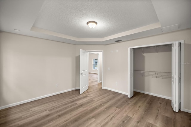 unfurnished bedroom with a raised ceiling, a closet, hardwood / wood-style floors, and a textured ceiling