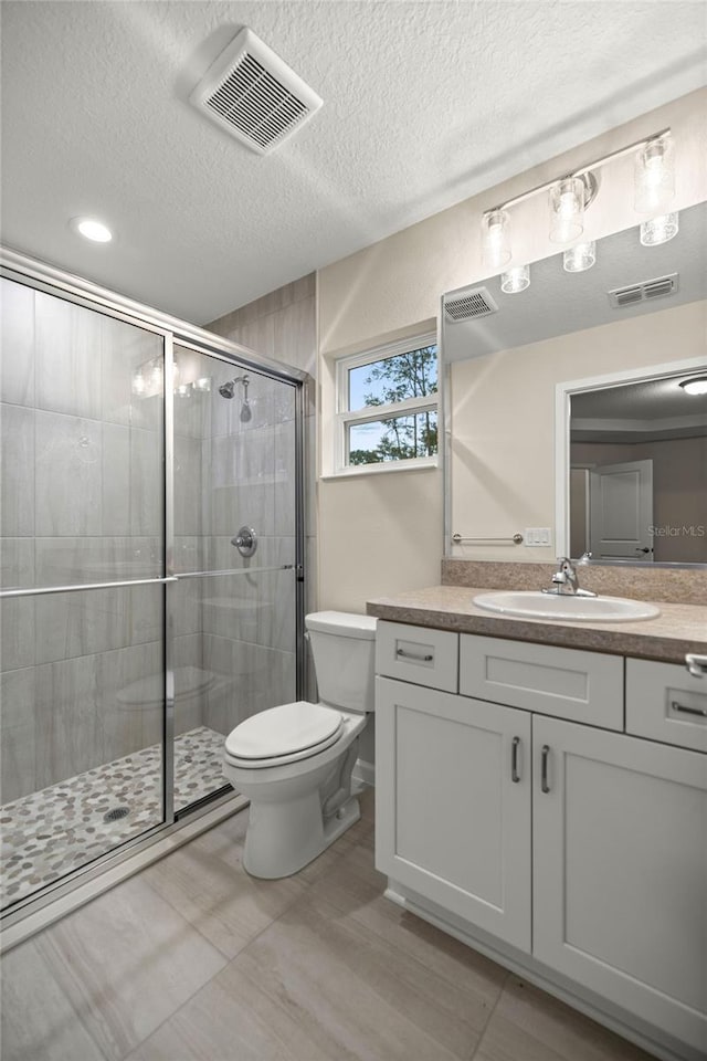 bathroom featuring toilet, a shower with door, vanity, and a textured ceiling