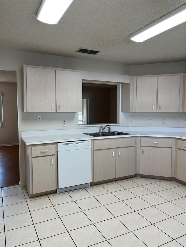 kitchen featuring a textured ceiling, light brown cabinetry, light tile patterned floors, white dishwasher, and sink