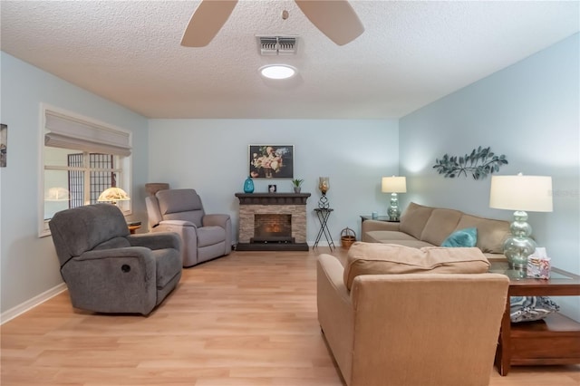 living room featuring light hardwood / wood-style floors, a textured ceiling, ceiling fan, and a fireplace