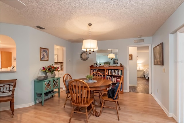 dining space with light hardwood / wood-style floors, a textured ceiling, and a notable chandelier