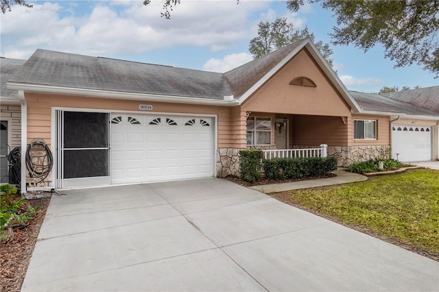 ranch-style house with covered porch, concrete driveway, an attached garage, a front yard, and stone siding