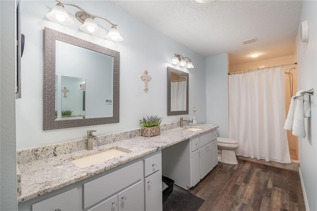 9051 SW 96th Ln Unit B, Ocala, FL 34481 - bathroom featuring wood finished floors, double vanity, toilet, a textured ceiling, and a shower with shower curtain