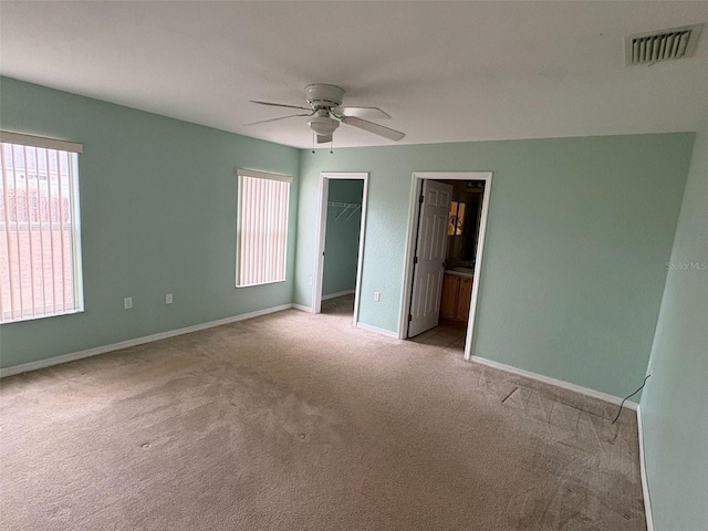 unfurnished bedroom with a spacious closet, ceiling fan, ensuite bath, a closet, and light colored carpet