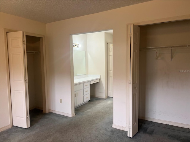 unfurnished bedroom featuring built in desk, a textured ceiling, dark carpet, a walk in closet, and a closet