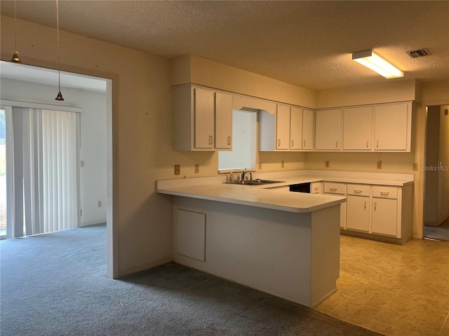 kitchen with pendant lighting, light countertops, white cabinetry, a sink, and a peninsula