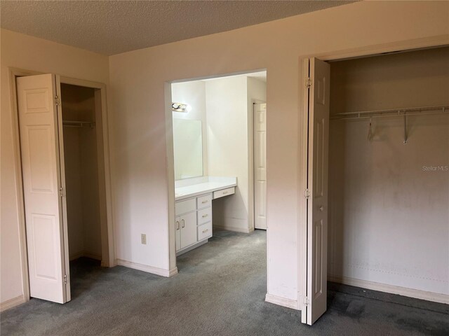 unfurnished bedroom featuring baseboards, a walk in closet, a textured ceiling, dark carpet, and a closet