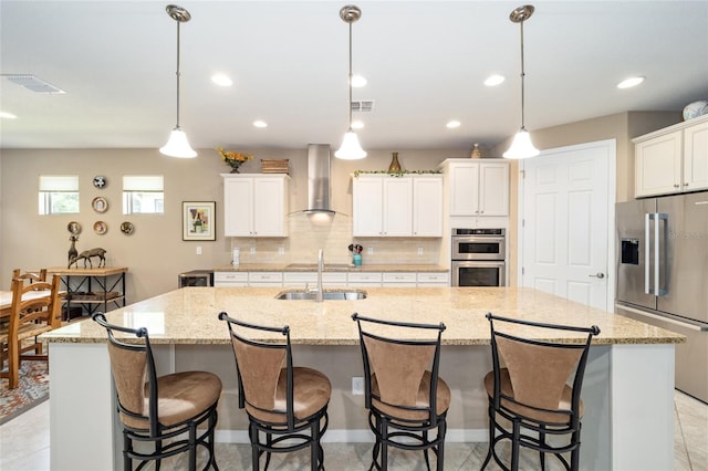 kitchen featuring a large island with sink, wall chimney range hood, hanging light fixtures, and appliances with stainless steel finishes