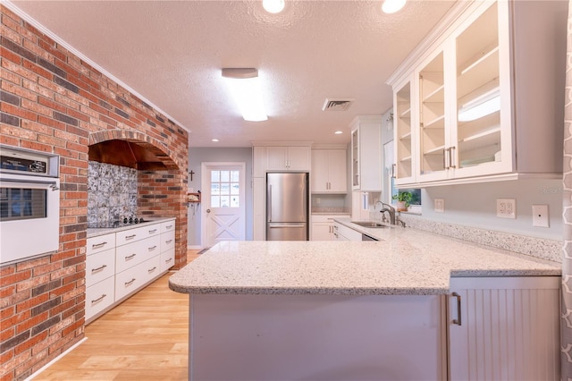 kitchen with oven, white cabinetry, a textured ceiling, kitchen peninsula, and stainless steel fridge