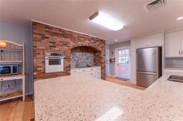 kitchen with light stone counters, a textured ceiling, stainless steel appliances, light wood-type flooring, and white cabinets