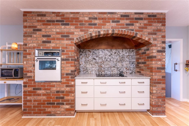 kitchen featuring white oven, black electric cooktop, light stone counters, white cabinets, and range hood