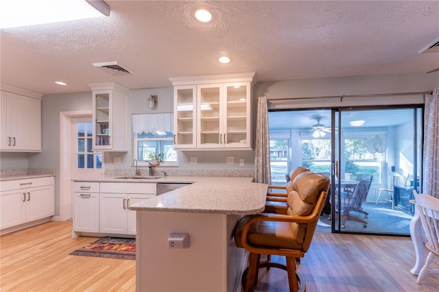 kitchen featuring a textured ceiling, white cabinetry, a breakfast bar area, light stone countertops, and plenty of natural light