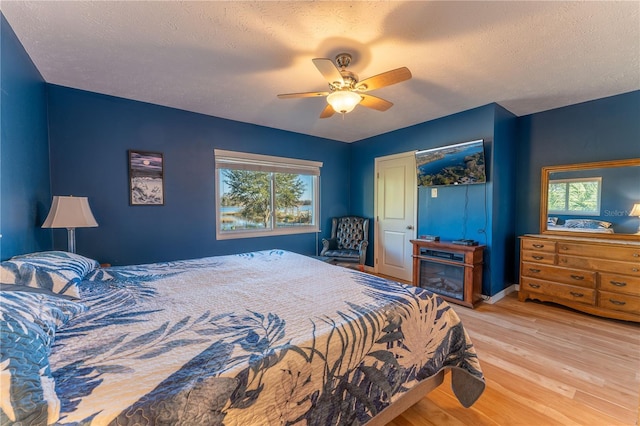 bedroom with ceiling fan, light hardwood / wood-style flooring, and a textured ceiling