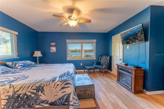 bedroom featuring light wood-type flooring, ceiling fan, a textured ceiling, and multiple windows