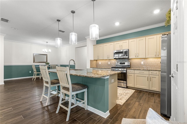 kitchen featuring appliances with stainless steel finishes, a kitchen breakfast bar, hanging light fixtures, ornamental molding, and a kitchen island with sink