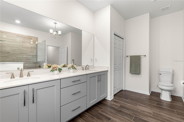 bathroom featuring toilet, vanity, a notable chandelier, and a tile shower