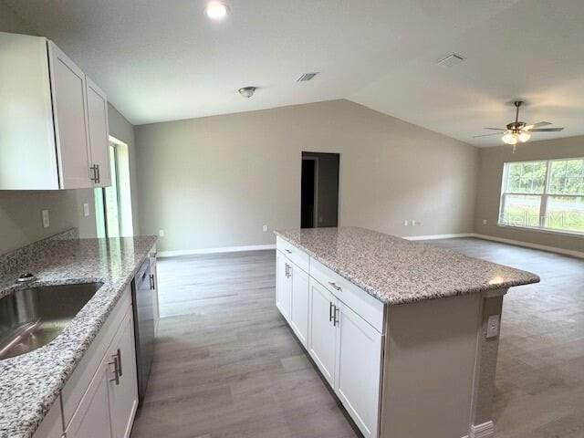 kitchen with light wood finished floors, open floor plan, dishwasher, vaulted ceiling, and a sink