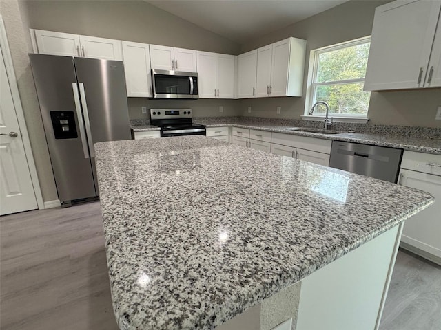 kitchen featuring a sink, white cabinetry, light wood-style floors, appliances with stainless steel finishes, and light stone countertops