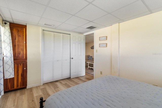 bedroom with light hardwood / wood-style floors, a paneled ceiling, and a closet