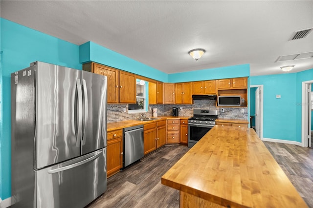 kitchen with sink, stainless steel appliances, dark hardwood / wood-style floors, wood counters, and decorative backsplash