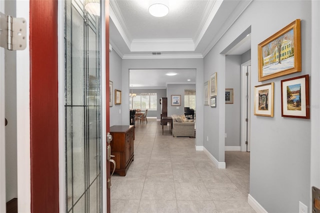 hallway featuring a tray ceiling, ornamental molding, a textured ceiling, light tile patterned floors, and a chandelier