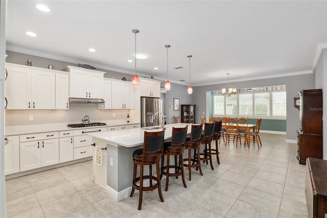 kitchen featuring appliances with stainless steel finishes, decorative light fixtures, a kitchen island with sink, ornamental molding, and white cabinets