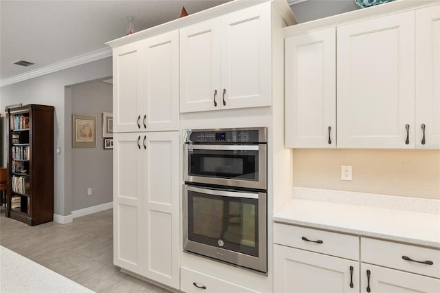 kitchen featuring decorative backsplash, crown molding, white cabinetry, light stone countertops, and double oven