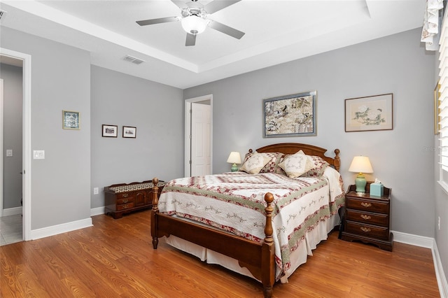 bedroom featuring ceiling fan, wood-type flooring, and a tray ceiling