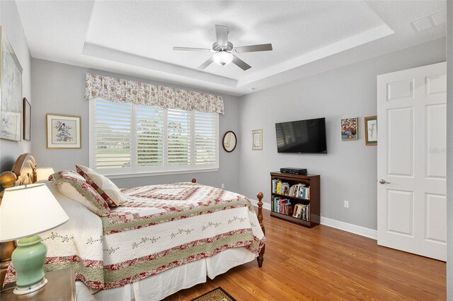 bedroom featuring ceiling fan, hardwood / wood-style flooring, and a tray ceiling