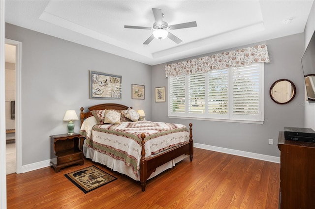 bedroom featuring ceiling fan, wood-type flooring, and a tray ceiling