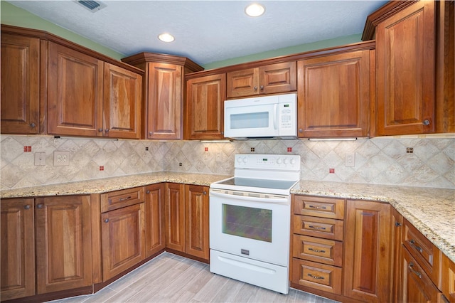 kitchen with tasteful backsplash, light stone countertops, white appliances, and light hardwood / wood-style flooring