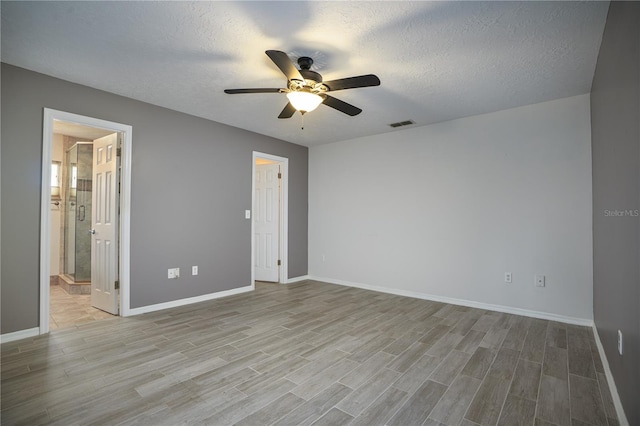 unfurnished bedroom with a textured ceiling, ceiling fan, light hardwood / wood-style flooring, and ensuite bath