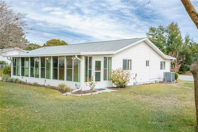 back of property with central AC unit, a sunroom, and a lawn