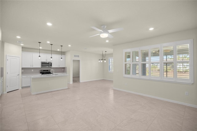 kitchen featuring a center island with sink, white cabinetry, hanging light fixtures, stainless steel appliances, and ceiling fan with notable chandelier