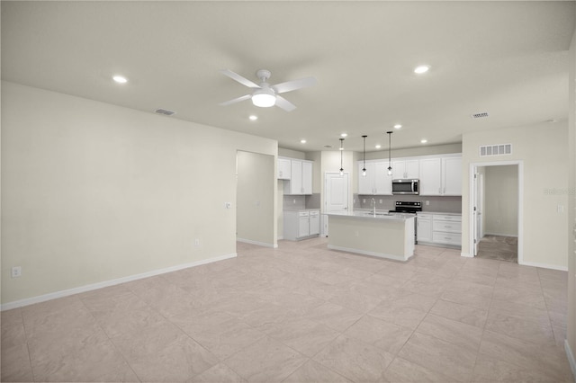 kitchen with an island with sink, appliances with stainless steel finishes, pendant lighting, white cabinets, and sink