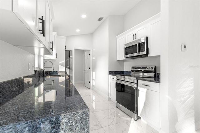 kitchen featuring appliances with stainless steel finishes, dark stone countertops, and white cabinets