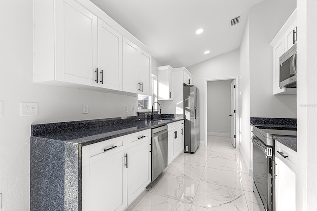 kitchen featuring appliances with stainless steel finishes, lofted ceiling, dark stone counters, white cabinets, and sink