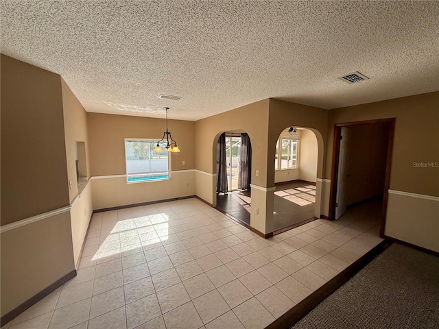 unfurnished room with light tile patterned floors, visible vents, arched walkways, and a textured ceiling