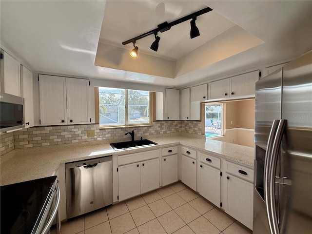 kitchen with a sink, light countertops, appliances with stainless steel finishes, decorative backsplash, and a raised ceiling