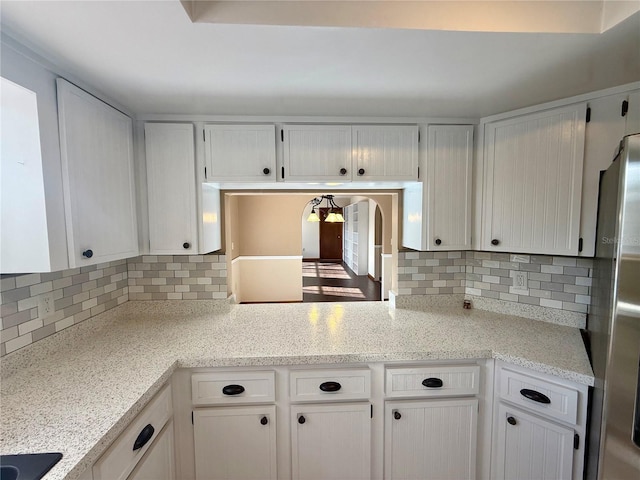 kitchen featuring decorative backsplash, freestanding refrigerator, and white cabinets