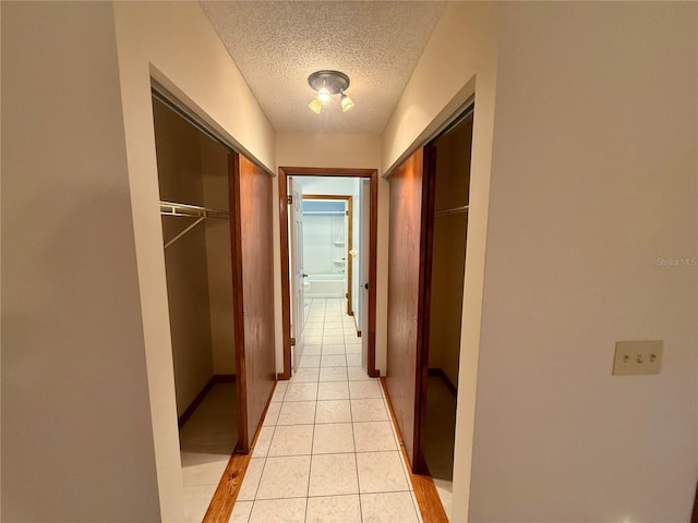 hallway with a textured ceiling, light tile patterned flooring, and baseboards