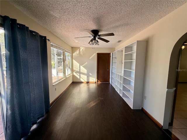 empty room featuring baseboards, arched walkways, a ceiling fan, wood finished floors, and a textured ceiling