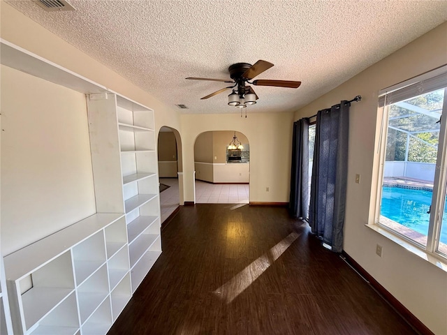 empty room featuring arched walkways, a textured ceiling, wood finished floors, a ceiling fan, and baseboards