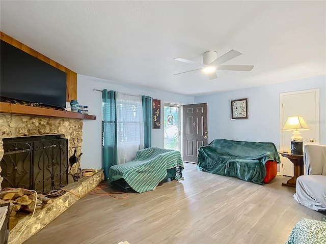 bedroom with ceiling fan, hardwood / wood-style floors, and a stone fireplace