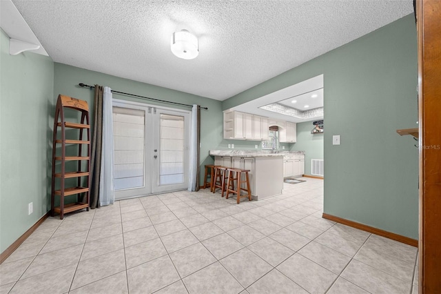 kitchen featuring french doors, light tile patterned flooring, a breakfast bar, a textured ceiling, and kitchen peninsula