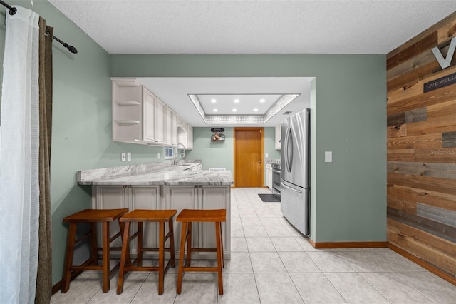 kitchen featuring stainless steel fridge, a breakfast bar area, white cabinetry, kitchen peninsula, and wood walls