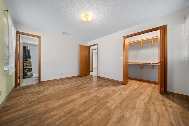 unfurnished bedroom featuring a textured ceiling, a closet, and light hardwood / wood-style flooring