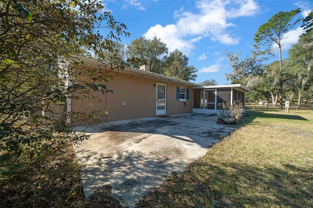 rear view of property featuring a lawn, a sunroom, and a patio