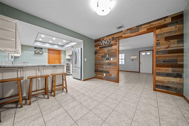 kitchen with appliances with stainless steel finishes, white cabinetry, a tray ceiling, a kitchen bar, and wood walls