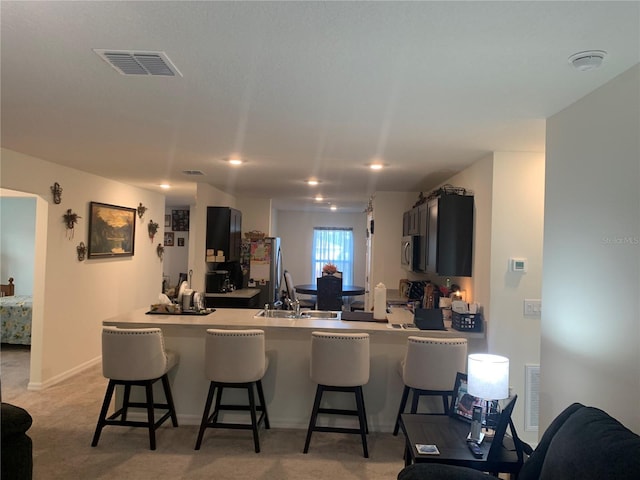 kitchen featuring sink, a breakfast bar area, light carpet, appliances with stainless steel finishes, and kitchen peninsula